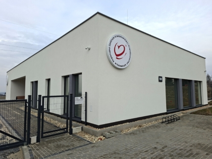 Nowoczesny, parterowy budynek Regionalnego Centrum Krwiodawstwa i Krwiolecznictwa z jasną elewacją. Na ścianie widoczne okrągłe logo RCKiK w Katowicach. Przed budynkiem chodnik z kostki, ogrodzenie oraz stojak na rowery.